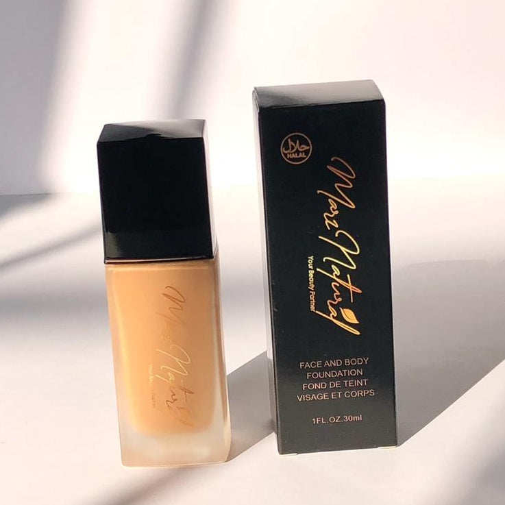 A bottle of liquid foundation next to its packaging box, with the brand name visible on the box. The bottle is filled with a beige-colored liquid, representing the 'Nude' shade of the product.