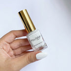 A hand holding a bottle of white balm nail polish with a shiny gold cap against a clean white background.