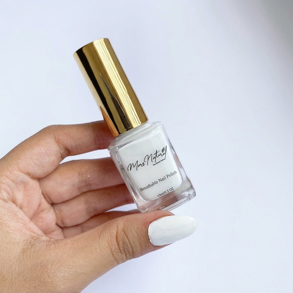 A hand holding a bottle of white balm nail polish with a shiny gold cap against a clean white background.