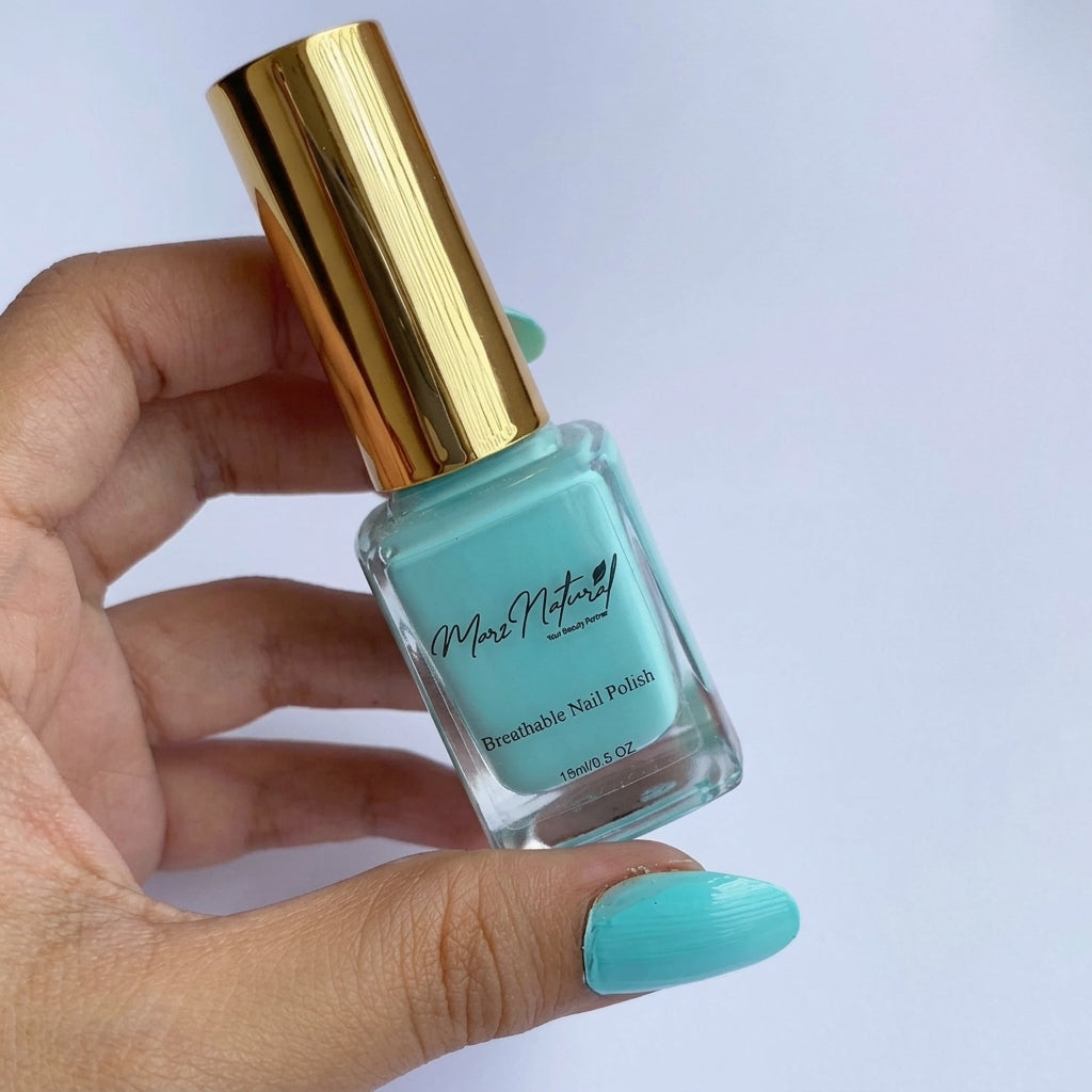 A hand holding a bottle of mint green nail polish with a shiny gold cap against a light background.