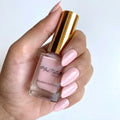 A hand holding a bottle of Marc Natalia Breathable Nail Polish in a light pink shade, with the hand's nails also painted in the matching pink polish against a clean white background.