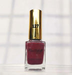 A bottle of Michelle Phillips nail polish in shade 127, featuring a metallic gold cap and a deep berry red polish inside a clear glass bottle, set against a bright, softly shadowed white background.