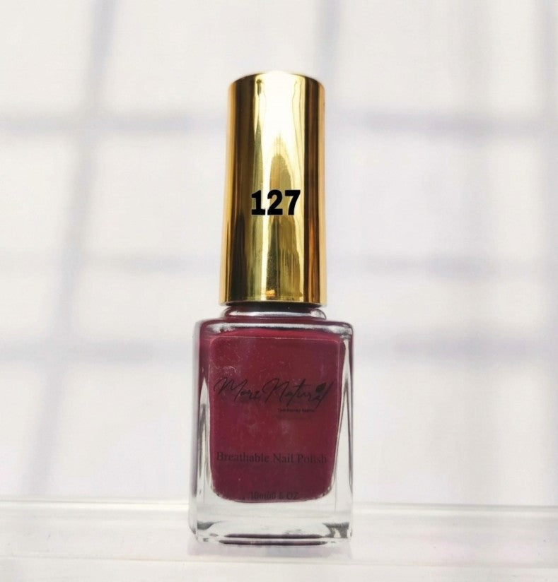 A bottle of Michelle Phillips nail polish in shade 127, featuring a metallic gold cap and a deep berry red polish inside a clear glass bottle, set against a bright, softly shadowed white background.