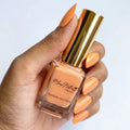 A hand holding a bottle of Marz Natural Breathable Nail Polish in a peach-orange shade, with the hand and fingernails also painted in the same color against a clean white background.