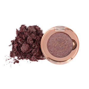 A pan of chromatic mirage eye shadow with a silvery Mocha, alongside loose eye shadow powder scattered outside the pan.