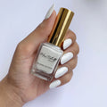 A hand with long, glossy white manicured nails holds a bottle of Mrs. and Mr.