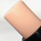 Close-up of a makeup stick or cream product tip showing a light peach-beige shade against a white background.