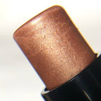 A close-up of a metallic bronze cosmetic stick, likely a highlighter or shimmer stick, showing its textured, shimmering copper-brown surface against a white background.